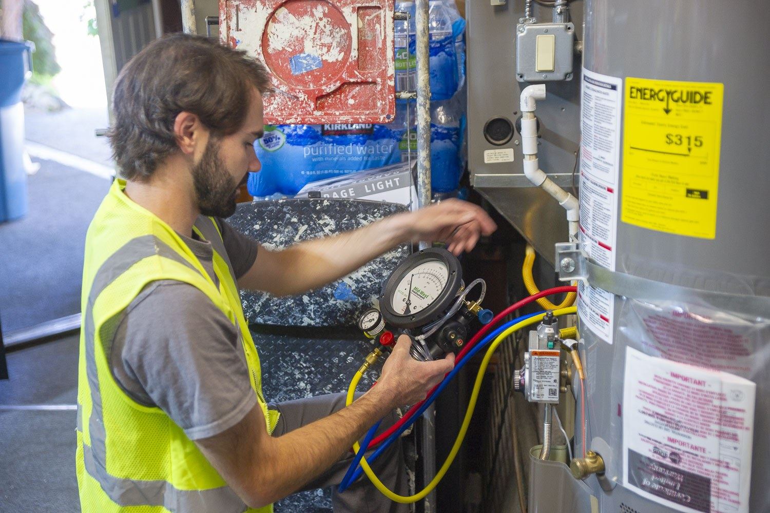 Technician reading a backflow test gauge beside a water heater